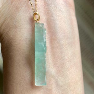 Peut inclure: Un collier &agrave; cha&icirc;ne dor&eacute;e avec un pendentif rectangulaire en jade vert clair. Le pendentif pr&eacute;sente des d&eacute;tails sculpt&eacute;s et une finition polie. Le collier est pr&eacute;sent&eacute; sur un fond de couleur chair.