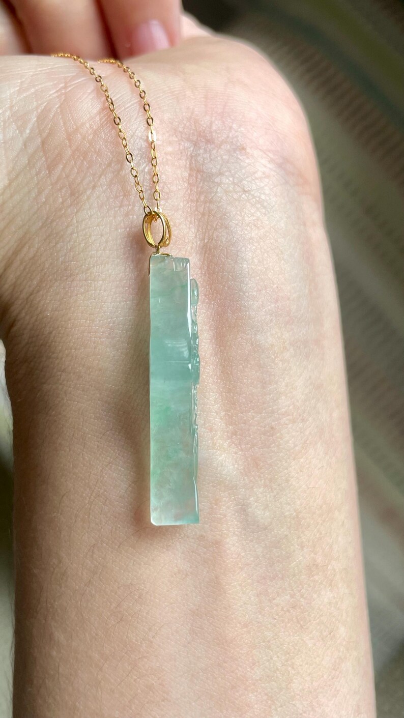 Peut inclure: Un collier &agrave; cha&icirc;ne dor&eacute;e avec un pendentif rectangulaire en jade vert clair. Le pendentif pr&eacute;sente des d&eacute;tails sculpt&eacute;s et une finition polie. Le collier est pr&eacute;sent&eacute; sur un fond de couleur chair.