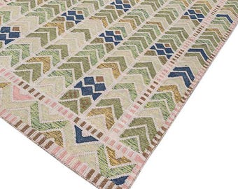 May include: A rectangular area rug with a geometric pattern. The rug features a repeating design of green, blue, and yellow arrow shapes on a beige background. Pink and brown borders frame the edges of the rug.