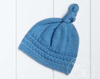 May include: A light blue knitted baby hat with a knotted top. The hat features a textured band near the brim. The word "Pattern" is in the top left corner. The hat is on a white wooden surface.