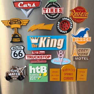 May include: A collection of colorful Cars movie-themed magnets. The magnets feature logos and text from the movie, including "Cars," "Rusteze," "Luigi's Tires," and "Route 66."