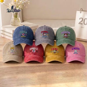 May include: A collection of seven baseball caps in various colors including blue, gray, green, tan, red, yellow, and pink. Each cap features embroidered text and a character graphic from The Amazing Digital Circus, including Zooble, Pomni, Ragatha, Jax, Gangle, Caine, and Kinger.