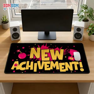 May include: Black rectangular mousepad with the words "NEW ACHIEVEMENT!" in yellow, with a pink bomb and trophy graphic. A white mouse and computer monitor are also visible. The mousepad is on a wooden desk.