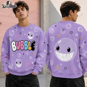 Puede incluir: Una sudadera de manga larga de color morado claro con la palabra BUBBLE en letras de colores en la parte delantera. El diseño incluye un patrón de burbujas blancas, puntos negros pequeños y estrellas amarillas. La espalda muestra una cara burbuja.