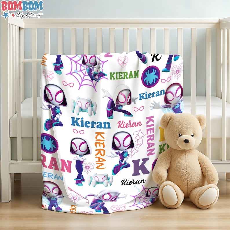 A teddy bear is sitting next to a white crib, with a colorful blanket featuring Spider-Man characters on it.