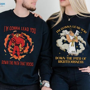 May include: Navy blue sweatshirts with matching graphics. One features a red cartoon figure with the text "I'M GONNA LEAD YOU DOWN THE PATH THAT ROCKS." The other shows an angel with the text "I'M GONNA LEAD YOU DOWN THE PATH OF RIGHTEOUSNESS."