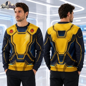 Op de afbeelding: Een sweatshirt met lange mouwen en ronde hals met een grafische print van een geel en donkerblauw harnasontwerp. De voorkant toont twee cirkelvormige rode accenten op het borstgedeelte. Het ontwerp bootst een futuristisch robot- of superheldenkostuum na.