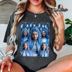 May include: A charcoal gray short-sleeve t-shirt featuring a graphic print of the name CHLOE in large blue letters. The design includes four repeating images of a person with long blue hair, arranged in a grid-like pattern on the front.