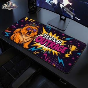 May include: A rectangular desk mat featuring a vibrant comic-book style illustration of an orange cat wearing a crown and purple sunglasses. The text "THIS IS AN OUTRAGE" is displayed in bold letters against a yellow starburst, with a gold trophy nearby.