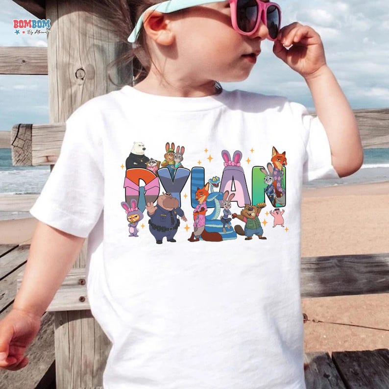 A child wearing a white t-shirt with a colorful graphic of cartoon characters and the name "Dylan" printed on it.