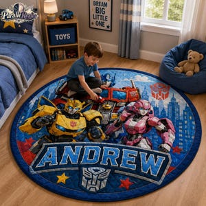Może przedstawiać: Okrągły niebieski dywan z grafiką Transformers przedstawiającą postacie Bumblebee, Optimus Prime i Arcee, panoramę miasta, imię ANDREW dużymi niebieskimi literami oraz logo Autobotów na pikowanym niebieskim tle.