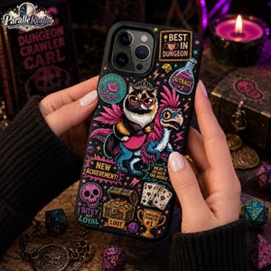 May include: A black smartphone case featuring a colorful graphic print of a cat wearing glasses and a crown riding a pink and blue creature. The design includes text such as BEST IN DUNGEON, NEW ACHIEVEMENT, and BITE-BUT-LOYAL, alongside icons of a skull, treasure chest, playing cards, and a trophy.