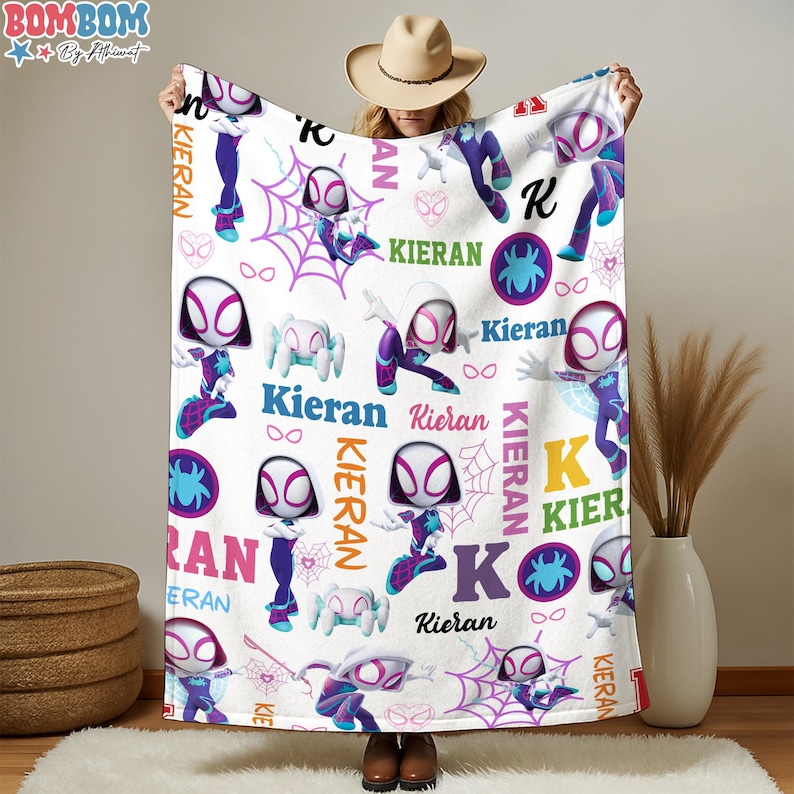 A person is holding up a blanket with a Spider-Man theme, featuring multiple Spider-Man characters and the name "Kieran" printed on it.