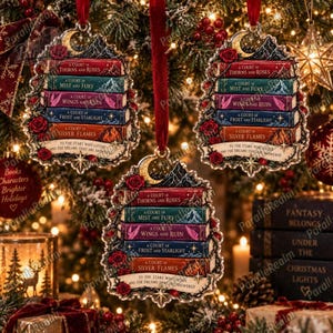 May include: Three identical Christmas tree ornaments shaped like a stack of five books with red velvet ribbons. Each ornament features the titles A Court of Thorns and Roses, Mist and Fury, Wings and Ruin, Frost and Starlight, and Silver Flames.