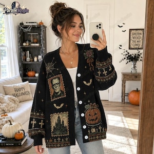 May include: A black V-neck cardigan featuring a button-down front and a Halloween-themed print. The design includes a portrait of Frankenstein's monster, a haunted castle, a jack-o'-lantern, spiderwebs, bats, and crosses in orange and brown tones.
