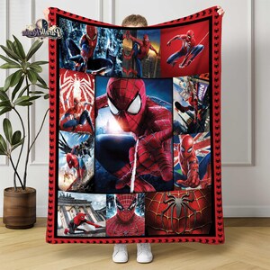 Puede incluir: Una manta roja y negra con tem&aacute;tica de Spider-Man que presenta m&uacute;ltiples im&aacute;genes del superh&eacute;roe en poses de acci&oacute;n. La manta tiene un borde rojo con iconos de ara&ntilde;as negras y un collage de im&aacute;genes de Spider-Man.