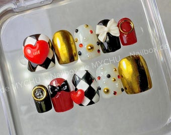 May include: A set of ten artificial nails with various designs. The nails feature a mix of colors, including gold, red, black, and white. Some nails have heart and bow accents, while others have a checkerboard pattern or gold embellishments. The nails are in a clear plastic case.