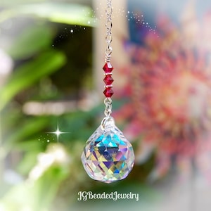 May include: A clear crystal ball pendant with a faceted surface hangs from a silver chain. Three red beads are strung above the crystal. The text "JGBeadedJewelry" is at the bottom.