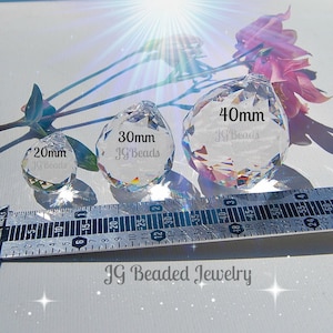 K&ouml;nnte beinhalten: Drei klare Kristallprismen-Anh&auml;nger in verschiedenen Gr&ouml;&szlig;en: 20 mm, 30 mm und 40 mm, mit dem Text "JG Beads" auf jedem. Ein Lineal ist unter den Prismen platziert. Das Bild enth&auml;lt auch rosa Blumen und den Text "JG Beaded Jewelry".