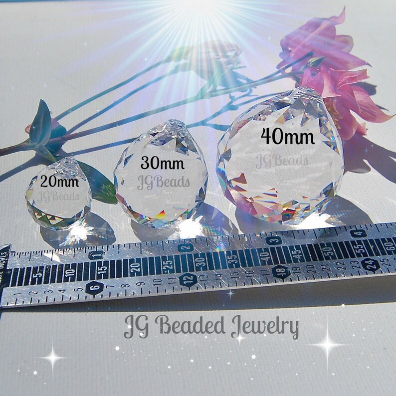 K&ouml;nnte beinhalten: Drei klare Kristallprismen-Anh&auml;nger in verschiedenen Gr&ouml;&szlig;en: 20 mm, 30 mm und 40 mm, mit dem Text "JG Beads" auf jedem. Ein Lineal ist unter den Prismen platziert. Das Bild enth&auml;lt auch rosa Blumen und den Text "JG Beaded Jewelry".