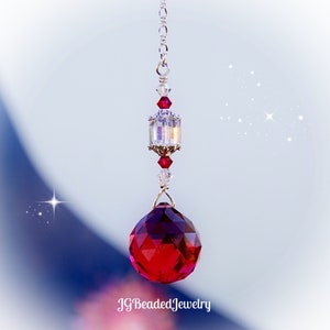Peut inclure: Un pendentif boule de cristal rouge foncé facetté est suspendu à une chaîne argentée. Le pendentif présente un cube de cristal clair et irisé et des accents de cristal rouge. Le texte "JGBeadedJewelry" est en bas.