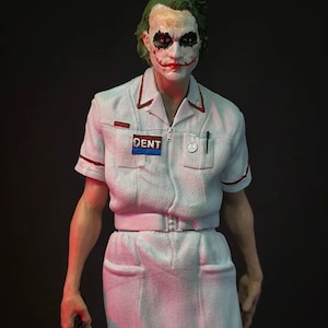 May include: A detailed figurine of a character with green hair, white face makeup, and red lipstick. The figure wears a white uniform with red trim and a "DENT" patch. A pen is in the pocket. The figure is holding a small object.