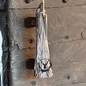 May include: A silver door handle shaped like a figure in a long robe holding a sword. The handle is mounted on a dark gray wooden door.