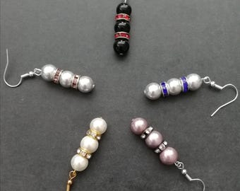 May include: Five drop earrings arranged in a circle, each featuring three spherical beads separated by two rhinestone-encrusted spacers. The set includes black with red crystals, silver with pink crystals, silver with blue crystals, white with clear crystals, and mauve with clear crystals.