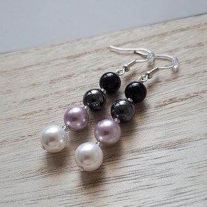 Könnte beinhalten: Ein Paar Hängeohrringe mit einem silbernen Haken und drei Perlen an jedem Ohrring. Die Perlen sind schwarz, grau und hellrosa.