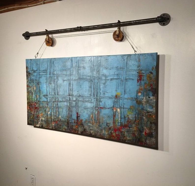 This painting has a grid pattern , a blue backround and multiple colors along the bottom in of red, green, mustard, orange. It is finished with a dark wash and hangs from a black iron pole that has a metal rope and rusted pulleys.Its highly textured.