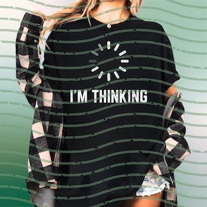 Puede incluir: Camiseta negra con el texto "I'M THINKING" y un gráfico de círculo de carga blanco. La camiseta se usa con una camisa de franela a cuadros en blanco y negro. El fondo tiene líneas onduladas verdes.