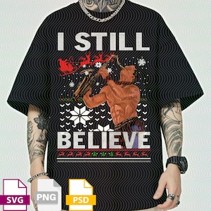 May include: Black t-shirt with a festive design. The graphic features a muscular figure playing a saxophone, a Santa's sleigh, snowflakes, and the text "I STILL BELIEVE" in white. The design has a Christmas sweater aesthetic.