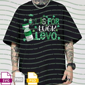 May include: Black t-shirt with green stripes and a St. Patrick's Day theme. The shirt features a graphic with a medicine vial, shamrocks, and the text "L is for Luck Levo".