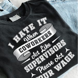 Puede incluir: Una camiseta negra con texto blanco que dice: I HATE IT When COWORKERS Act Like SUPERVISORS Please Act YOUR WAGE. El diseño incluye un gráfico de una cinta métrica envuelta alrededor de la palabra COWORKERS en una fuente de estilo bloque.