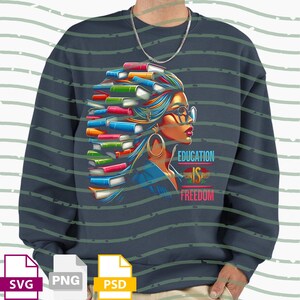 Op de afbeelding: Marineblauwe sweatshirt met een kleurrijke illustratie van een vrouw met boeken als haar, een bril en grote oorringen. De tekst "EDUCATION IS FREEDOM" is weergegeven in levendige kleuren.