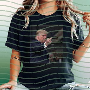 May include: Black t-shirt featuring a photographic image of a man in a suit, raising his middle finger. The image is centered on the shirt. The shirt has a crew neck and short sleeves.