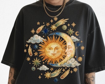 May include: A charcoal black oversized t-shirt featuring a central graphic print of a golden sun and a crescent moon with faces, surrounded by colorful stars, comets, and clouds. The design is arranged in a circular pattern on the front chest.