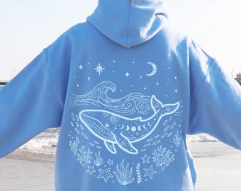 Peut inclure: Un sweat-shirt à capuche bleu clair avec un motif graphique en lignes blanches au dos. Le dessin représente une baleine entourée de vagues, de coraux, d'étoiles de mer et de petits poissons, avec un croissant de lune et des étoiles au-dessus.