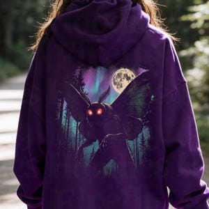 May include: A deep purple hooded sweatshirt featuring a large graphic on the back. The print depicts a dark, winged creature with glowing red eyes standing in a forest under a full moon and purple aurora borealis. The text Firefly Hoodies is visible.
