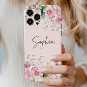 May include: Blush-colored phone case with a floral design featuring pink roses and green leaves. The name "Sophia" is written in cursive. The case is a snap case.