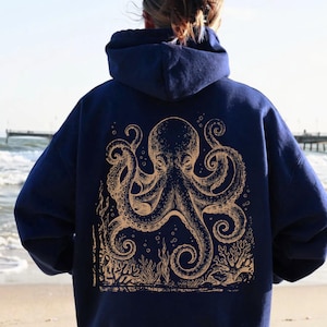 Könnte beinhalten: Marineblauer Kapuzenpullover mit einem goldenen Oktopus-Design auf dem Rücken. Die Oktopus-Illustration umfasst Tentakel, Blasen und Korallen. Der Hoodie hat eine Kapuze und lange Ärmel, ideal für Freizeitkleidung.