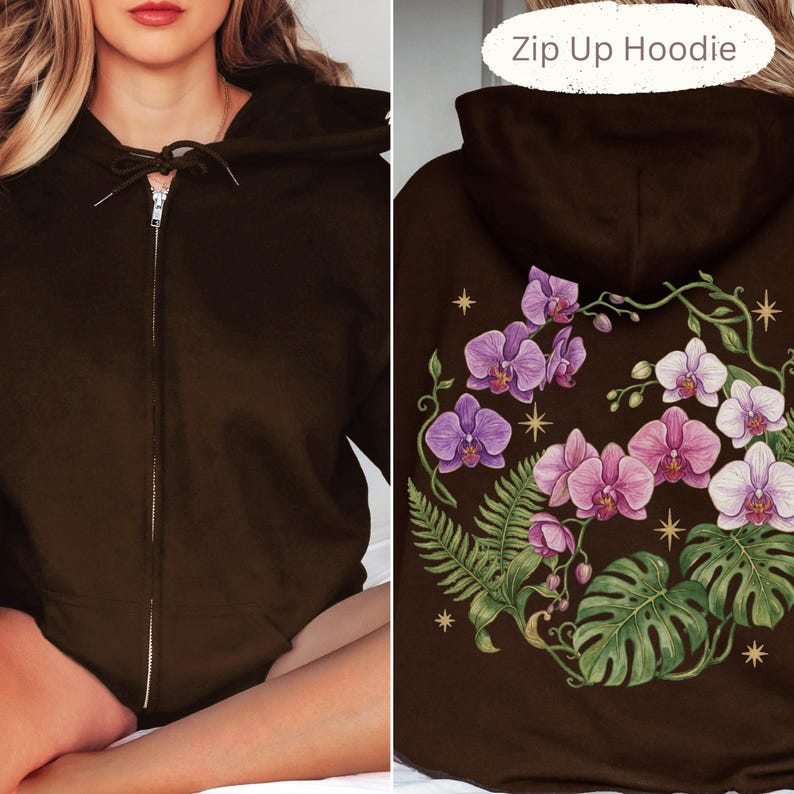 Puede incluir: Una sudadera con capucha y cremallera de color marr&oacute;n oscuro, con cordones y cremallera plateada. La parte posterior muestra un estampado gr&aacute;fico de orqu&iacute;deas moradas y blancas, hojas de helecho, hojas de monstera y estrellas doradas.