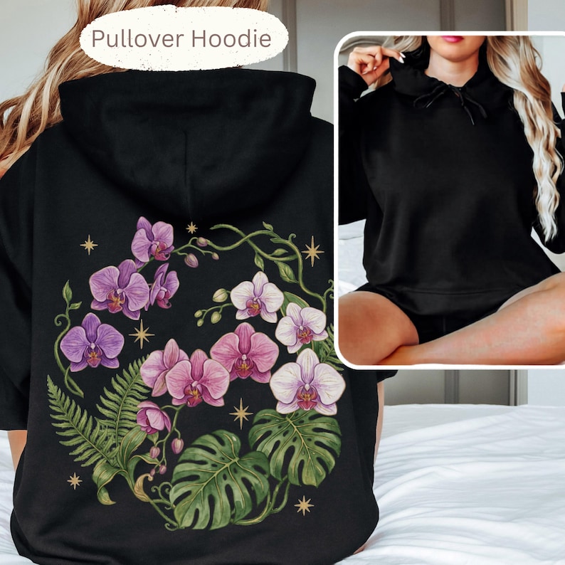 Puede incluir: Una sudadera con capucha negra que presenta un gran gr&aacute;fico en la espalda de orqu&iacute;deas moradas y blancas, frondas de helecho verdes y hojas de monstera acentuadas con peque&ntilde;as estrellas doradas. El frente es negro liso con capucha.