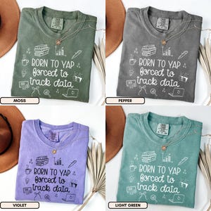 May include: Four t-shirts in moss, pepper, violet, and light green. Each shirt has the text "BORN TO YAP forced to track data" with graphic icons. A gold necklace is on each shirt.