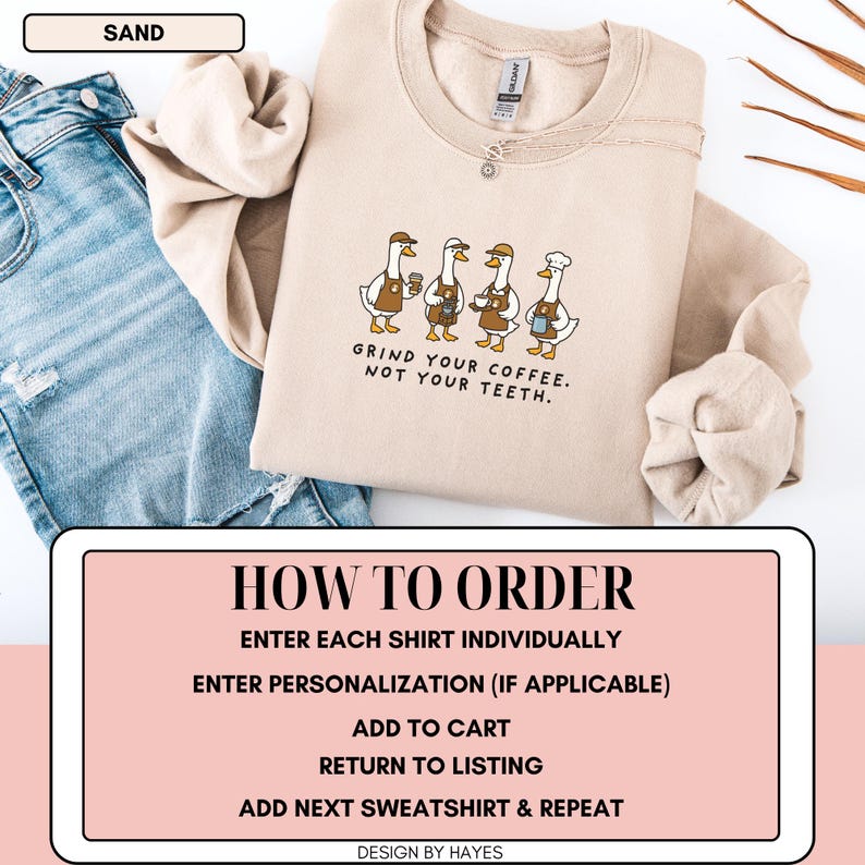 May include: A sand-coloured sweatshirt with a crew neck. The front displays a graphic of four cartoon geese holding coffee cups, with the text "GRIND YOUR COFFEE. NOT YOUR TEETH." The sweatshirt is shown with blue jeans.