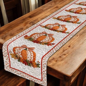 May include: A quilted table runner featuring a repeating pattern of orange pumpkins adorned with checkered bows and autumn leaves. The runner has a white background with a wavy stitched texture and is bordered by a thin orange trim.