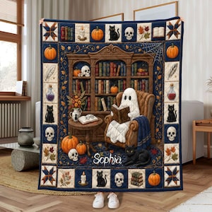 May include: A rectangular quilt featuring a central illustration of a ghost reading a book in a brown armchair within a library. The border displays pumpkins, skulls, black cats, and books. The name Sophia is printed in white script at the bottom.