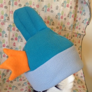 May include: A blue and light blue fleece hat with an orange felt fin on top. The hat is on a white mannequin head.