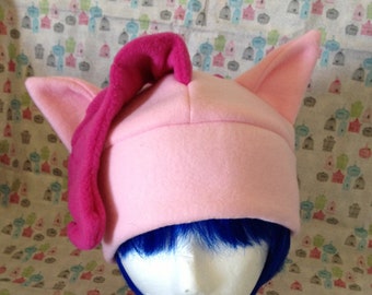 May include: Pink fleece hat with a pink curled ear and two pink ear flaps. The hat is on a mannequin head with blue hair.
