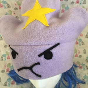 May include: Purple fleece Lumpy Space Princess hat with a yellow felt star and embroidered black facial features. The hat is shown on a mannequin head with bright blue wig.